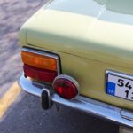 Rear bumper of vintage automobile with license plate and shadow on urban roadway in sunlight