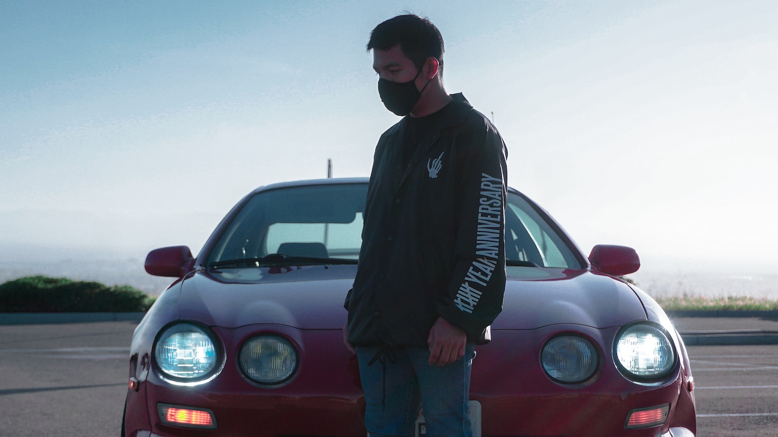 man in black jacket standing beside red car