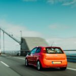 an orange car driving on a bridge with a bridge in the background