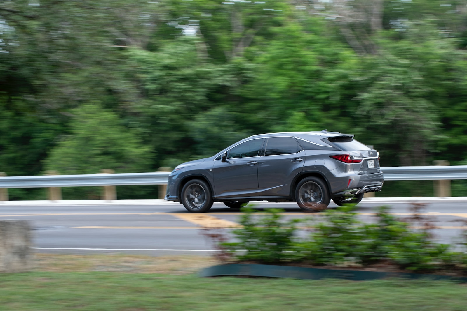 a gray car driving down a road next to a forest